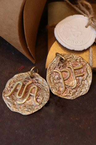 Colgante rústico con dos iniciales en latón. Hecho artesanalmente en España por Sandra Bellew.