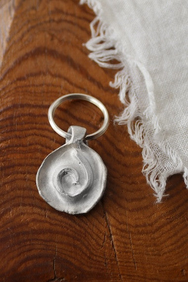 Llavero rústico con imagen de una espiral en plata. Hecho artesanalmente en España por Sandra Bellew.