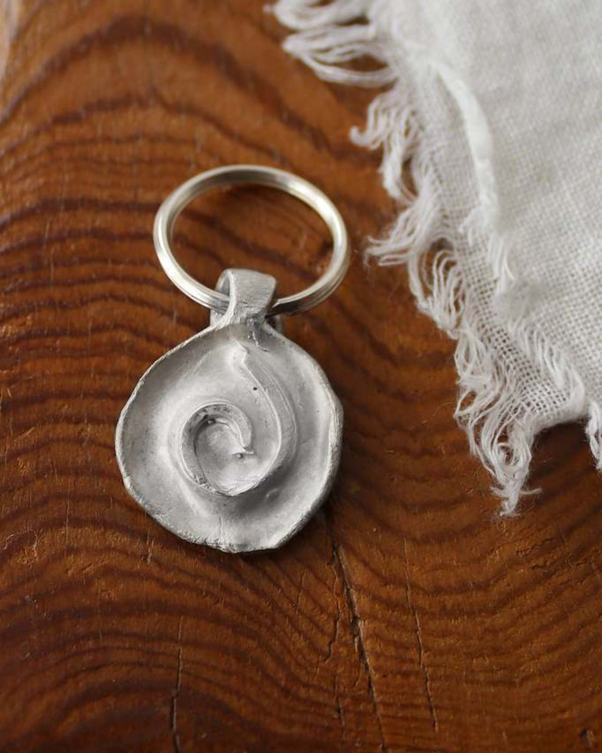 Llavero rústico con imagen de una espiral en plata. Hecho artesanalmente en España por Sandra Bellew.